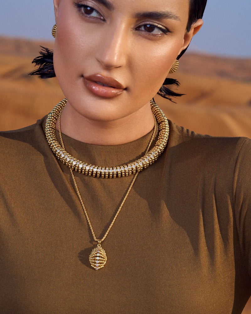 Woman wearing gold necklaces against a desert background
