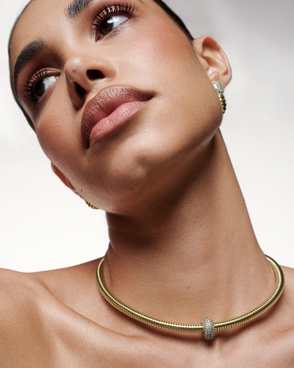 A gold statement necklace with ribbed detailing and subtle sparkle, designed to elegantly contour the neckline