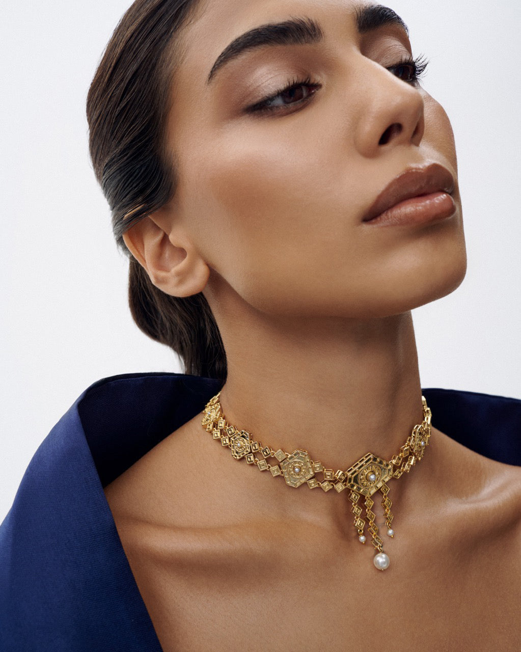 Woman wearing a gold necklace with a pearl pendant on a plain background